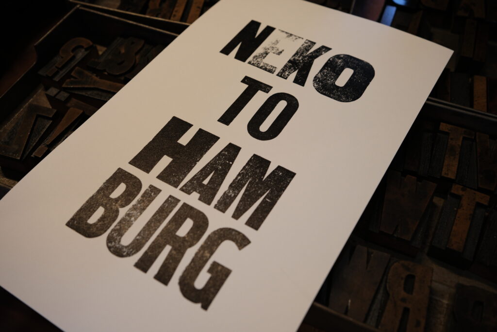 NINE LETTERPRESSの木活字ワークショップで制作したNEKOTOHAMBURGの活版印刷作品。黒い文字にカスレやインキの濃淡が見える